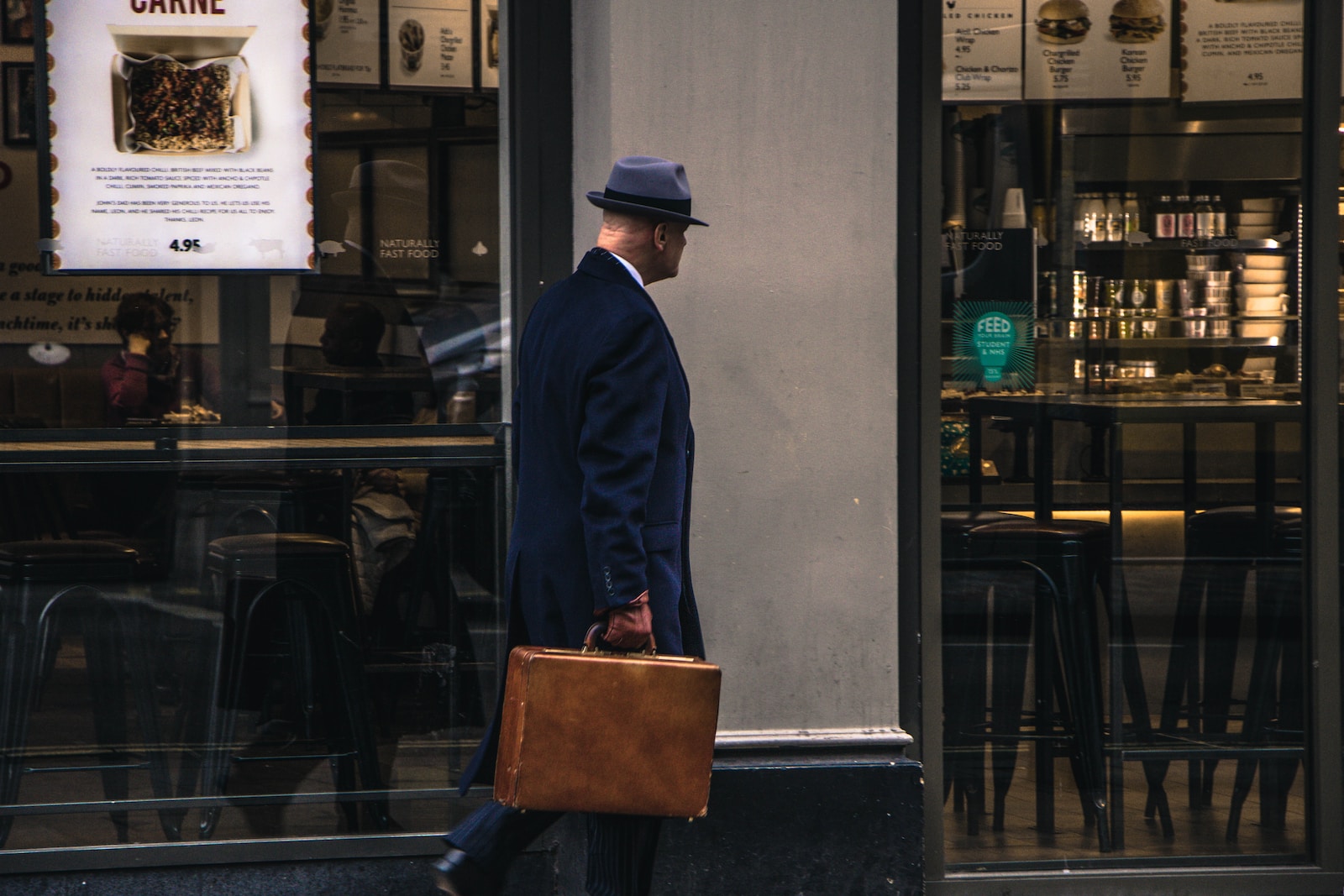 man in black suit jacket and blue hat standing in front of store